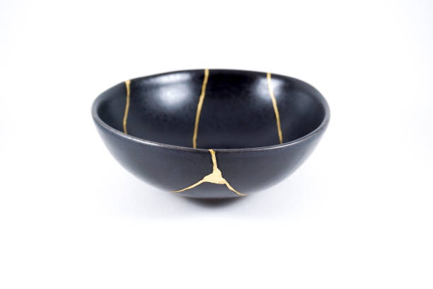 Isolated black Japanese kintsugi bowl, antique pottery restored with gold cracks. Traditional gold fixing method. stock photo
