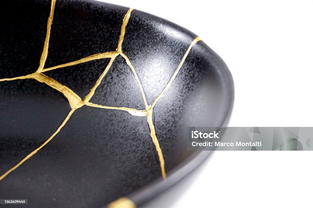 Isolated black Japanese kintsugi bowl, antique pottery restored with gold cracks. Traditional gold fixing method. kintsugi gold cracks restoration, Japanese black bowl fixed with the antique kintsukuroi restoration technique, the beauty of imperfections, representation of a trauma Kintsugi Stock Photo