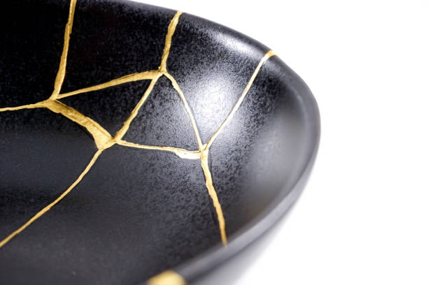 Isolated black Japanese kintsugi bowl, antique pottery restored with gold cracks. Traditional gold fixing method. stock photo