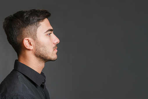Close-up profile view portrait of young handsome serious guy on gray background. High quality photo, copy space