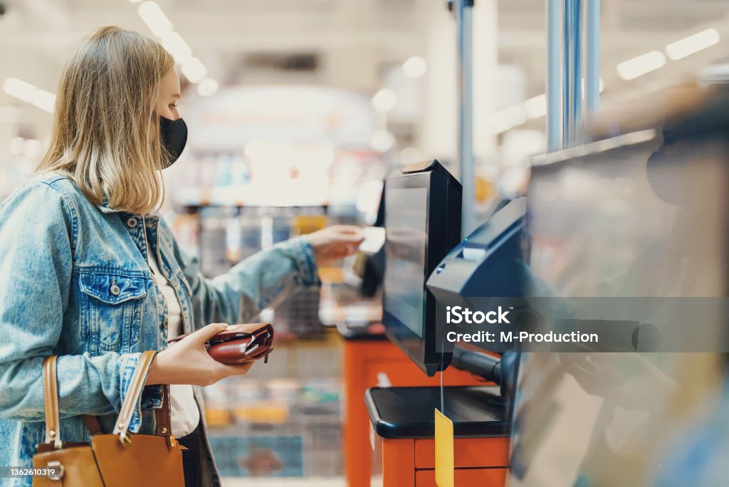 Woman in medical mask pays at self-checkouts. 35-39 Years Stock Photo