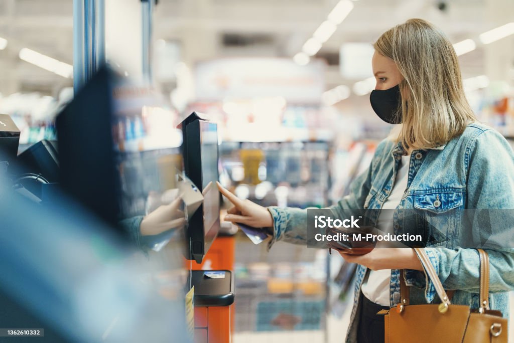 Woman in medical mask pays at self-checkouts. Self Service Stock Photo