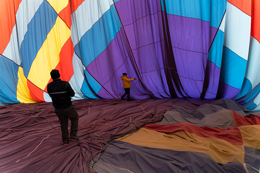 sıcak hava balonu yere iniş yaptıktan sonra balonun içine giren işçi ipleri çekerek çadırı toplamaktadır. işçinin çalışırken siluet görüntüsü full frame makine ile çekilmiştir.