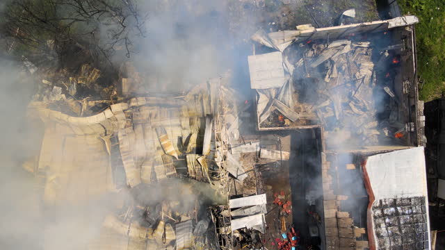 Aerial view of ruined building on fire with collapsed roof and rising dark smoke