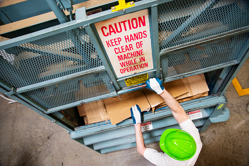 An employee using an industrial compactor in a factory, store or warehouse.  An occupational health and safety topic.