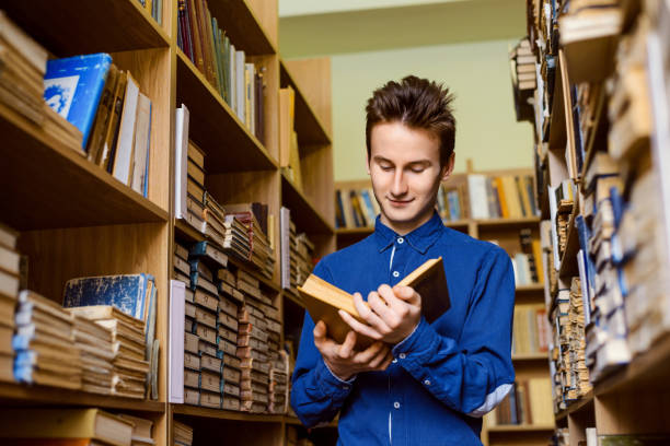 istock Happy student with a book in his hands in the library 1362611816