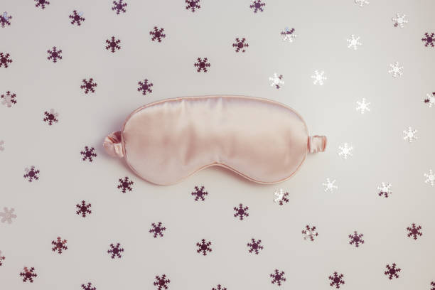 istock Pink satin eye sleeping mask on winter background with snowflakes 1362613124