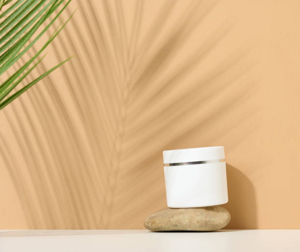 istock white round plastic jar for cosmetic products on a brown background. Palm leaf shadow. Blank for branding products, mock up 1362618291