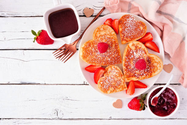 Valentines or Mothers Day heart shaped pancakes. Top down view on a white wood background with copy space.