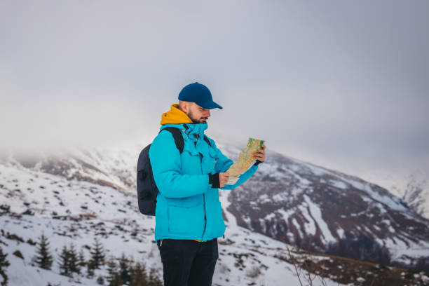 istock Young male hiker wearing a blue jacket and a backpack is looking at the map with snowy mountains in the background 1362623607