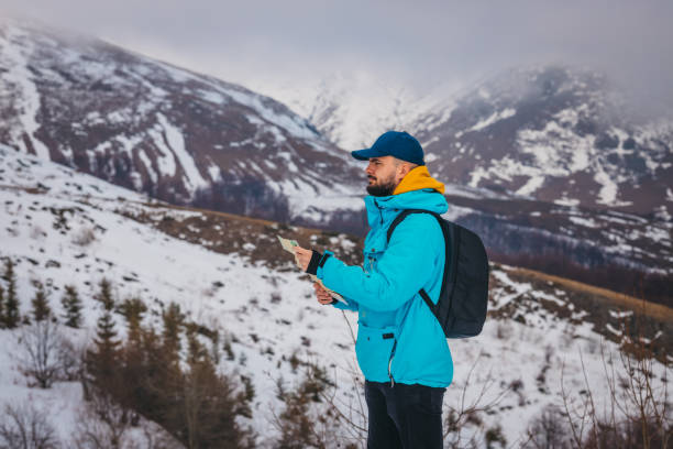 un jeune randonneur portant une veste bleue et un sac à dos regarde la carte avec des montagnes enneigées en arrière-plan - trail marker hiking sign sports and fitness photos et images de collection