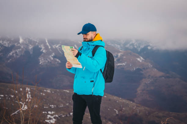 un jeune randonneur portant une veste bleue et un sac à dos regarde la carte avec des montagnes enneigées en arrière-plan - trail marker hiking sign sports and fitness photos et images de collection