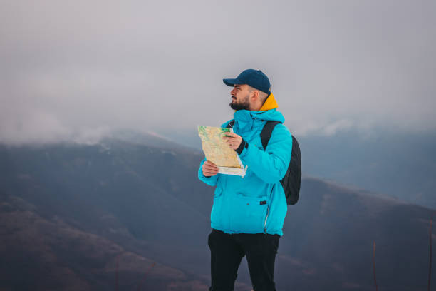 istock Young male hiker wearing a blue jacket and a backpack is looking at the map with snowy mountains in the background 1362624116
