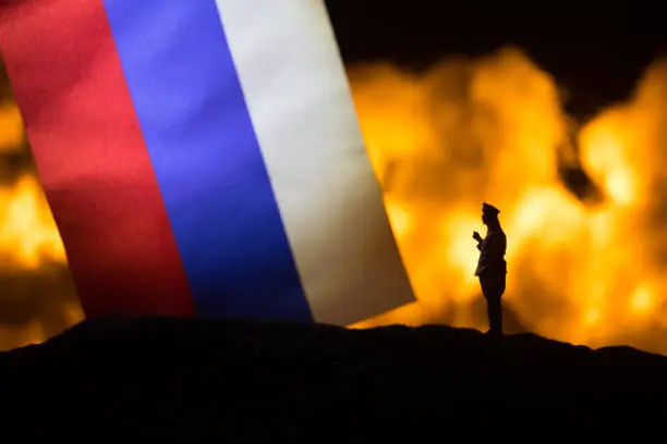 Russia flag on burning dark background. Concept of crisis of war and political conflicts between nations. Silhouette of armed soldier against a Russian tricolor. Selective focus