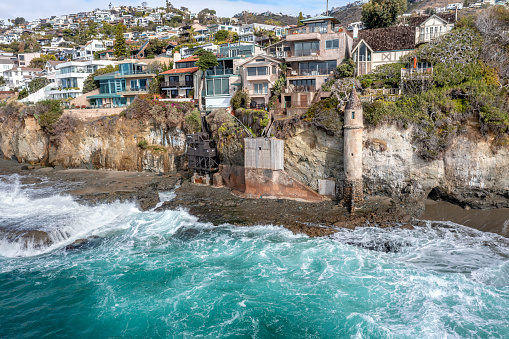 Aerial view of Victoria Beach with the famous pirate's Tower, an area of Orange County California for the wealthy and affluent, shows the crashing waves as they roll over jagged shoreline reefs.