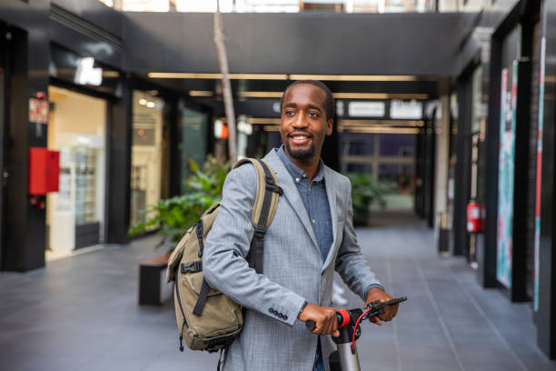 африканский бизнесмен со своим электрическим скутером. улыбающийся парень элегантно одетый идет на работу с экологически чистым транспор� - nonpolluting стоковые фото и изображения