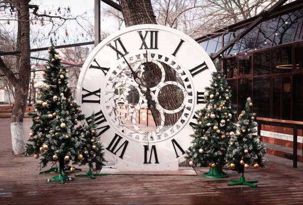 um grande relógio de madeira branco redondo com numerais romanos. cinco minutos às doze da manhã. cinco minutos para meia-noite. relógio de natal. parque de natal. decorações de rua de natal no parque - 12 oclock - fotografias e filmes do acervo