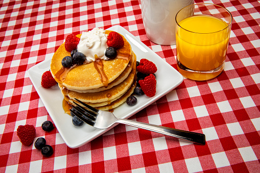 This is a photograph of a large tall stack of pancakes on a checkered table cloth in the studio