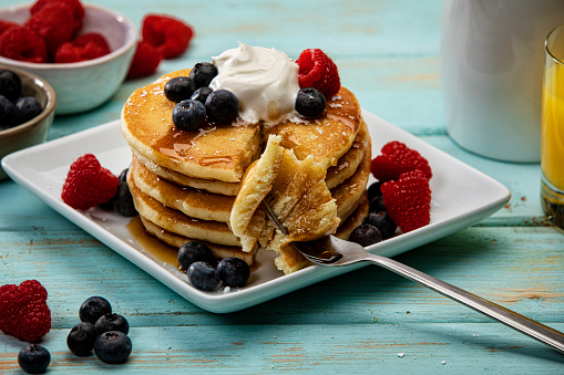 This is a photograph of a large tall stack of pancakeson a blue wood background