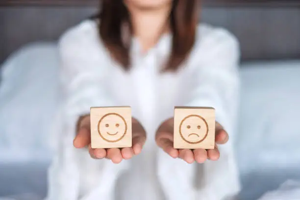 Photo of Woman holding smile and angry emotion face block. Customer choose Emoticon for user reviews. Service rating, mental health, positive thinking, satisfaction, evaluation and feedback concept
