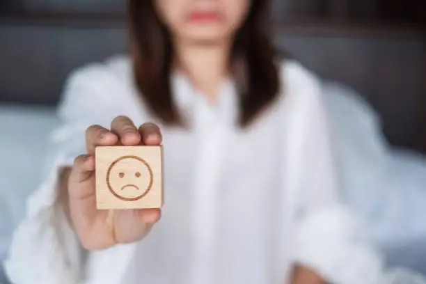 Photo of Woman holding angry emotion face block. Customer choose Emoticon for user reviews. Service rating, mental health, positive thinking, satisfaction, evaluation and feedback concept