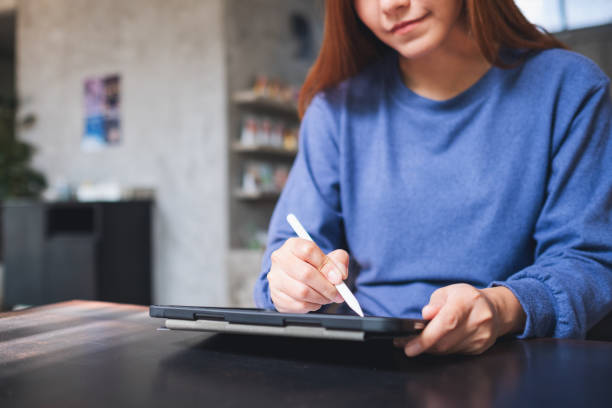 Closeup of a young woman using smart pen technology for working and writing on digital tablet screen stock photo