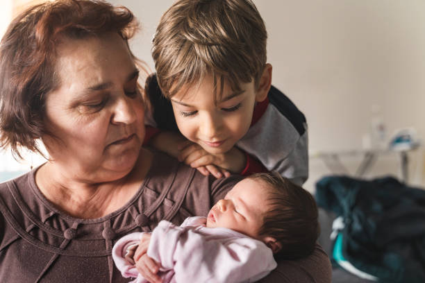 bebê pequeno caucasiano recém-nascido menina yawing nas mãos de sua avó enquanto seu irmão mais velho está observando-a - vínculo familiar e novo conceito de vida - baby grandparent newborn grandmother - fotografias e filmes do acervo