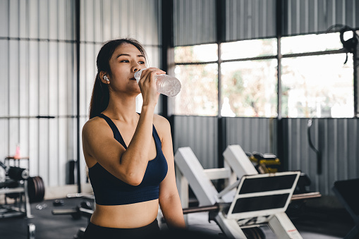 Asian young woman drinking water after workout in gym, healty and sport concept