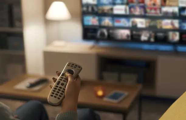 Young woman relaxing on the couch at home and watching videos on demand on her TV, entertainment concept