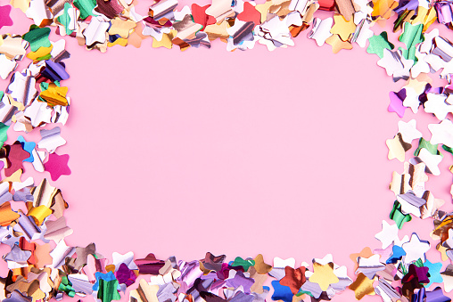 Bright colorful star-shaped confetti sparkles on a pink background, copy space, the theme of a holiday and a birthday.