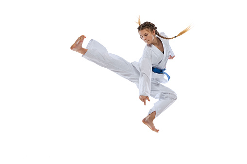 Jumping kick. Portrait of young girl, teen, taekwondo athlete practicing alone isolated over white background. Concept of sport, education, skills, workout, healthy lifestyle and ad. Power and energy.