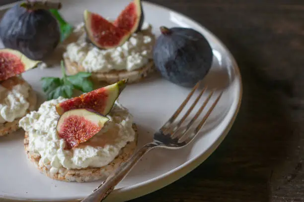 Delicious open faced sandwiches made with brown rice cracker, cottage cheese and figs. Served on a plate isolated on wooden table. High protein, guten free and vegetarian meal or snack