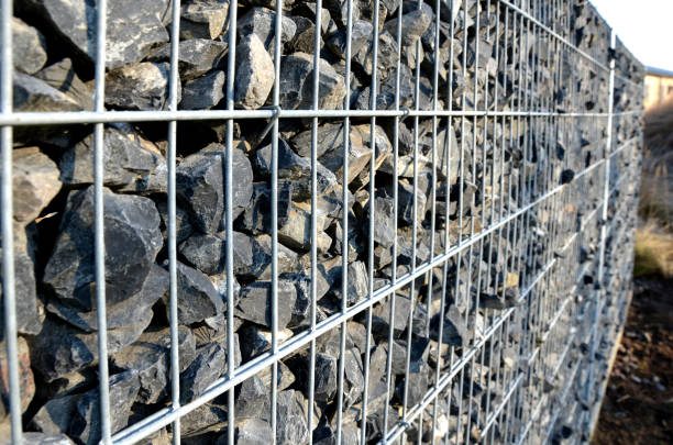 2つのワイヤースラブの間に注がれたフェンシングホーム粗い砂利の一部として、ガビオン擁壁の建設。網のメッシュの間を覗く石 - gabion wall ストックフォトと画像