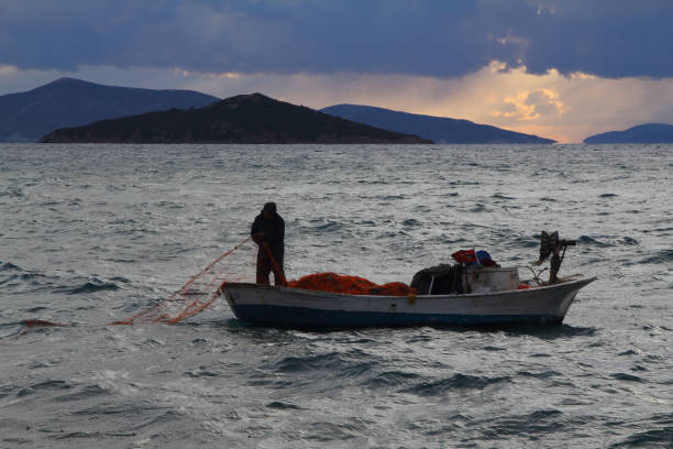 Paros, Greece - November 21, 2009: Greek Fishermen bringing in their boat and unloading their nets to the small dock on Island of Paros on the Aegean sea.