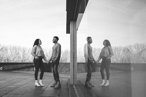 Young multiethnic couple in love. Interracial couple embrace reflected in a glass surface. Monochrome version.