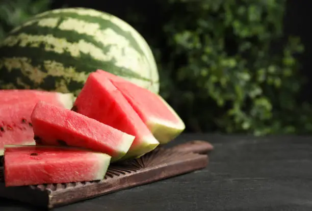 Whole and cut ripe watermelons on black table. Space for text