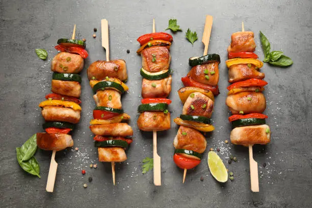 Delicious chicken shish kebabs with vegetables and herbs on grey table, flat lay