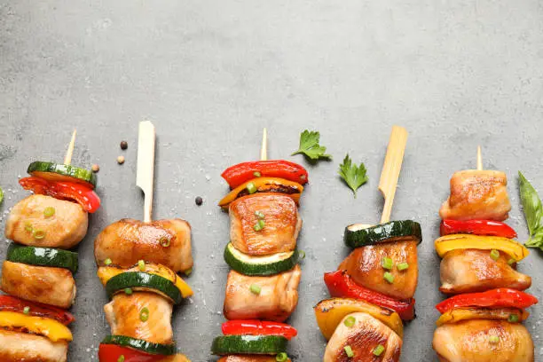 Delicious chicken shish kebabs with vegetables and herbs on grey table, flat lay. Space for text