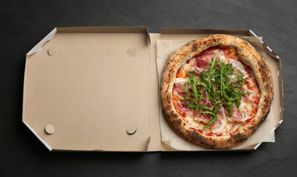 istock Tasty pizza with meat and arugula in cardboard box on black table, top view 1362688542