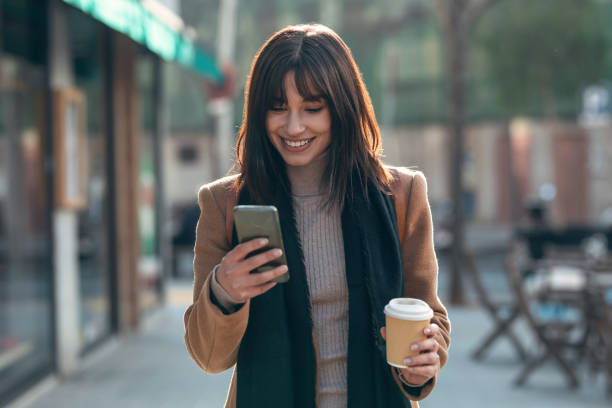 istock Pretty young woman using her mobile phone while drinking cup of coffee walking the streets of the city. 1362695655