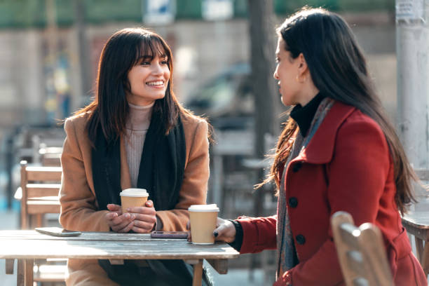 istock Two attractive friends enjoying coffee together while talking and laughing sitting on the terrace of a bar. 1362695750