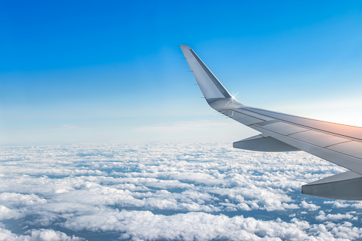 White aircraft wing above the clouds on blue sunrise sky. View from airplane window.  Beautiful and peaceful air travel and transportation concept. Copy space.