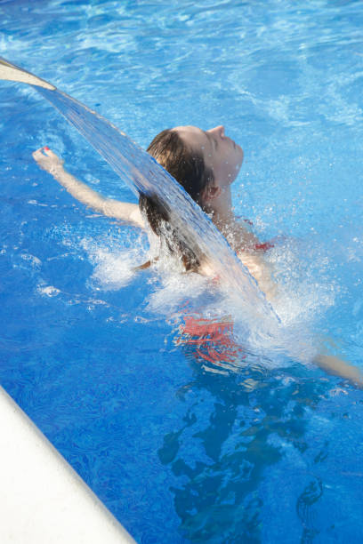 istock Young woman relaxing under swimming pool waterfall jet 1362702621