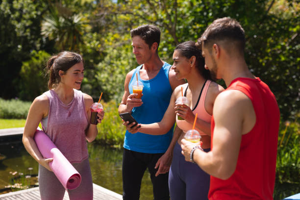 Men and women in sportswear having healthy drinks post workout in park. healthy lifestyle, drink and fitness.