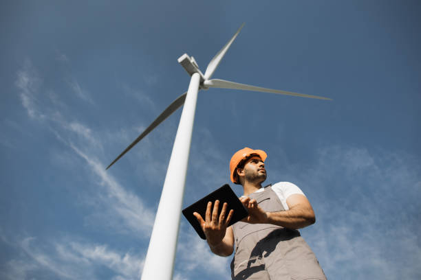 istock Indian engineer standing among windmill farm with tablet 1362712575