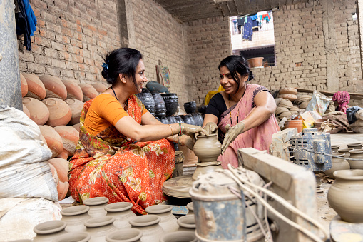Two women working on potters wheel making a clay pot.