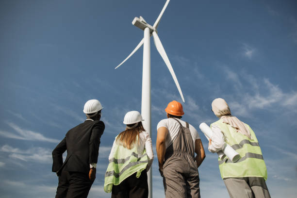 istock Multicultural partners in helmets looking on wind turbine 1362713620