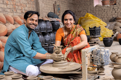 Portrait of happy Indian couple potters shaping the clay into pot on spinning wheel