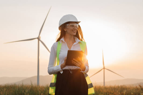 une femme casquée travaillant avec une tablette à une ferme d’énergie renouvelable - working windmill photos et images de collection