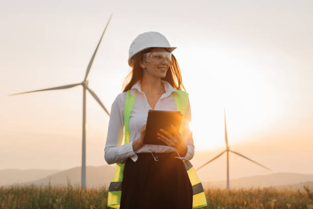 Woman in helmet working with tablet at renewable energy farm Beautiful caucasian woman in white helmet working with digital tablet at renewable energy farm. Female inspector controlling functioning of wind turbines outdoors. engineer stock pictures, royalty-free photos & images